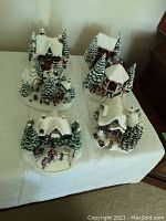 Overview photo showing four of the six ceramic Christmas village buildings with snow and pine tree decorations.