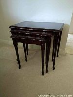 Set of three dark mahogany nesting tables stacked together showing overall shape and scale.