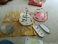 Full view of the luncheon set items spread on beige carpet including two-tier Royal Wessex petite four server, Aynsley pink platter with handle, clear stemware, luncheon plates, and small trays.