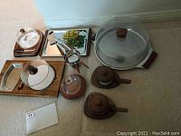 Overview of assorted mid-century tabletop serving items including wooden trays, ceramic condiment servers with lids, metal trays, and a glass dome cheese dish.