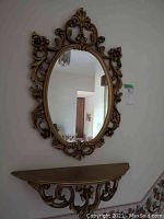 Frontal view of gold-colored ornate oval wall mirror hung on wall above shelf