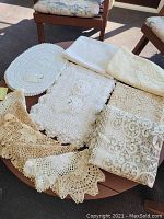 Overview of assorted lace and crochet table linens arranged on a table, showing various folded cloths, oval doily, and patterns