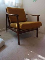 Front right three-quarter view of teak frame chair with mustard yellow seat and back cushions