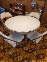 Front perspective showing round card table with vinyl top and four matching metal chairs with vinyl seats and backs.