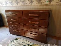 Front view of the maple dresser showing eight drawers with rectangular wooden handles and lower scalloped base detail.