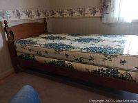 Full view of twin maple bed frame with floral mattress side view showing headboard and mattress thickness.