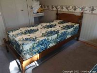 Photo showing twin bed with maple wood frame and floral patterned mattress in bedroom setting.