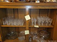 Two wooden shelves filled with clear crystal stemware on top shelves and assorted glass candy dishes and bowls on bottom shelf