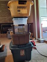 Stacked four plastic storage totes and a laundry basket. Largest bottom tote is blue Rubbermaid Roughneck HiTop 5-stage.