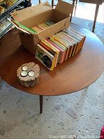 Photo showing round wooden mid century coffee table with box of paperback books and a wooden tea light holder on top, table leg visible