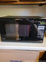 Front view of black Panasonic microwave oven with digital keypad and display panel, showing overall condition and size.