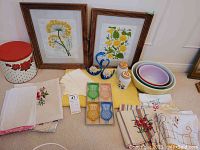 Wide shot of entire lot showing all the items arranged on floor including linens, Pyrex bowls, glass swans, salt & pepper shakers, thistle dishes, framed prints and storage tin.