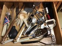 Top drawer with measuring spoons, ladle, pastry cutters, ice cream scoops, metal slotted spoon and other kitchen utensils.