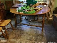 Full view of the wooden drop leaf table with chairs around it and items on top showing the table structure and legs.