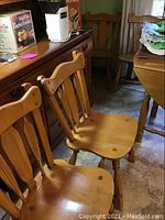 Four wooden kitchen chairs arranged closely together showing their front and side profiles. Chairs have warm honey finish and contoured seats.