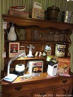 Photo showing wooden buffet with various kitchen items including electric fondue pot, boxes for mixer and popcorn popper, miscellaneous jars, excluded figurines