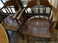 Two wooden captain's chairs side by side by a window, showing full profile of armrests and back supports.