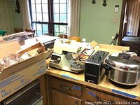Photo showing white stand mixer with bowl, stainless steel rice cooker, toaster, and other kitchen items on countertop.