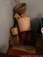Photo showing stacked wicker and woven baskets of various shapes and sizes in corner by wall