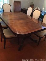 Full view of the rectangular wooden dining table with a pedestal base and upholstered chairs around it, highlighting shape and style.