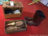 Full view of shoeshine wooden box, wooden shoe forms in box, and cowboy boots side by side on carpet