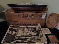 Assembled model ship displayed on original box with instruction booklet in front. Shows ship hull painted black and brown with white trim, mounted on a black display stand. Instruction booklet titled "Sea Witch" visible with black and white illustrations of ship.