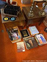 45 rpm vinyl records organized in a black metal rack, two 45s laid flat, boxes with vinyl LP records, and stacks of sheet music on an orange carpeted floor.
