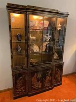 Full front view of the black display cabinet showing three glass door sections with interior shelves and lights and decorated lower cabinets.