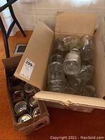 Open cardboard box filled with multiple clear glass mason jars and several loose metal lids.