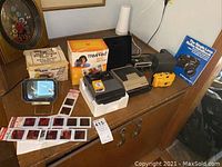 Photo of vintage cameras, slide viewer, boxes, and photographic slides on wooden dresser