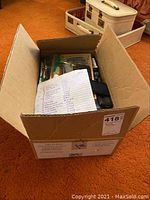 Photo of an open cardboard box filled with various knife boxes and knives inside, listing includes a paper note on top.