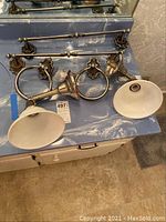 Photo showing two bathroom light fixtures with frosted glass shades, two towel bars, and two towel ring holders all in brushed metal finish with decorative mounts.
