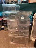 Nine stacked clear acrylic storage boxes of various sizes and two shallow trays on top. One box cracked as per seller description.