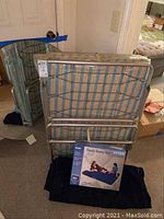 Metal folding cot shown folded and standing against a door with two folded mattresses behind.