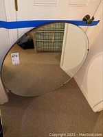 Full view of large circular mirror leaning against a door, showing clear reflective surface and thin frame.