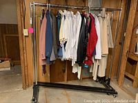 Full view of a metal rolling garment rack holding men's suit jackets, dress shirts, and ties hung on hangers.