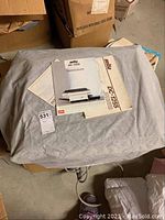 Mita DC-1255 office copier under protective cloth in basement storage area, with instruction manuals placed on top.