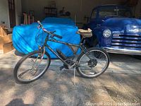 Full side view of the Huffy Manitoba mountain bike showing frame, tires, and attached accessories in garage setting.