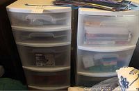 Two plastic storage drawers side by side filled with office supplies and assorted items.