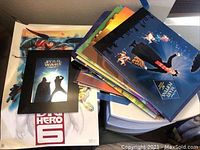 Top view showing a pile of colorful posters and lithographs including Star Wars Trilogy framed lithograph and Big Hero 6 poster.