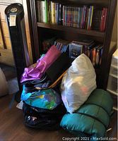 39-inch tower fan and a pile of assorted large bags, including a pink patterned tote, blue-green gym bag, and white plastic bag of clothing.