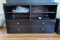 Front angle view of wooden TV stand showing four drawers and open shelves above them with items inside.