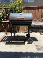 Full view of large Char-Griller BBQ smoker with side firebox, wheels, folding shelves, and lower storage rack standing outdoors.