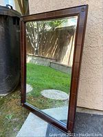 Photo shows one of the Bombay Company hanging mirrors leaning against an outdoor wall, reflecting grass and pavement.
