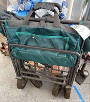 Folded wagon in green fabric and black metal frame with four wheels and mesh storage pockets on the side.