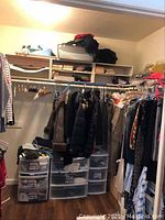 Closet corner with six plastic drawer units below hanging clothes, three melamine shelves mounted on wall above, some clothes on hangers visible but not included