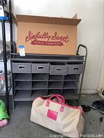 Photo shows the PVC and metal shoe rack with four gray fabric drawers, multiple cubby shelves, a beige and pink travel bag in front, and some shoes on the floor.