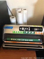 FoodSaver vacuum sealer machine with control panel and sealing area visible, rolls placed behind the machine.