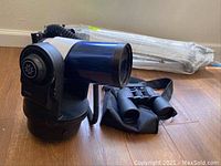 Overview of telescope optical tube on mount, wrapped tripod in background, and binoculars in case