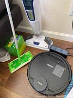 Photo showing the Deebot robotic vacuum, Bissell PowerFresh vacuum, and Swiffer dry sweeper with charger beside them on wooden floor